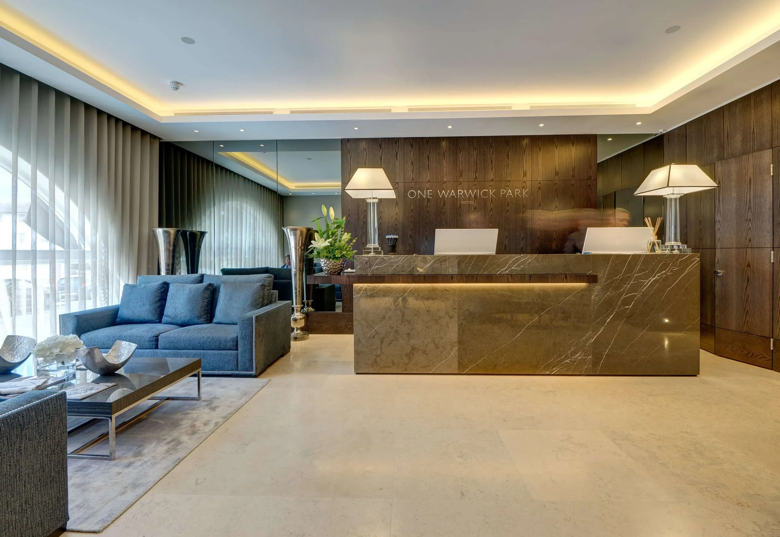 Modern One Warwick Park Hotel lobby with marble reception desk, blue sofa, wood-paneled walls, and stylish lamps