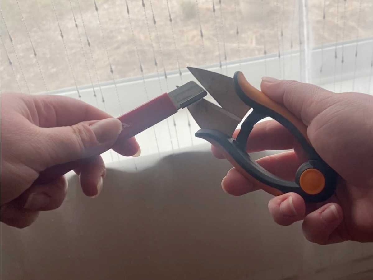 Plant clippers being sharpened with a tool.