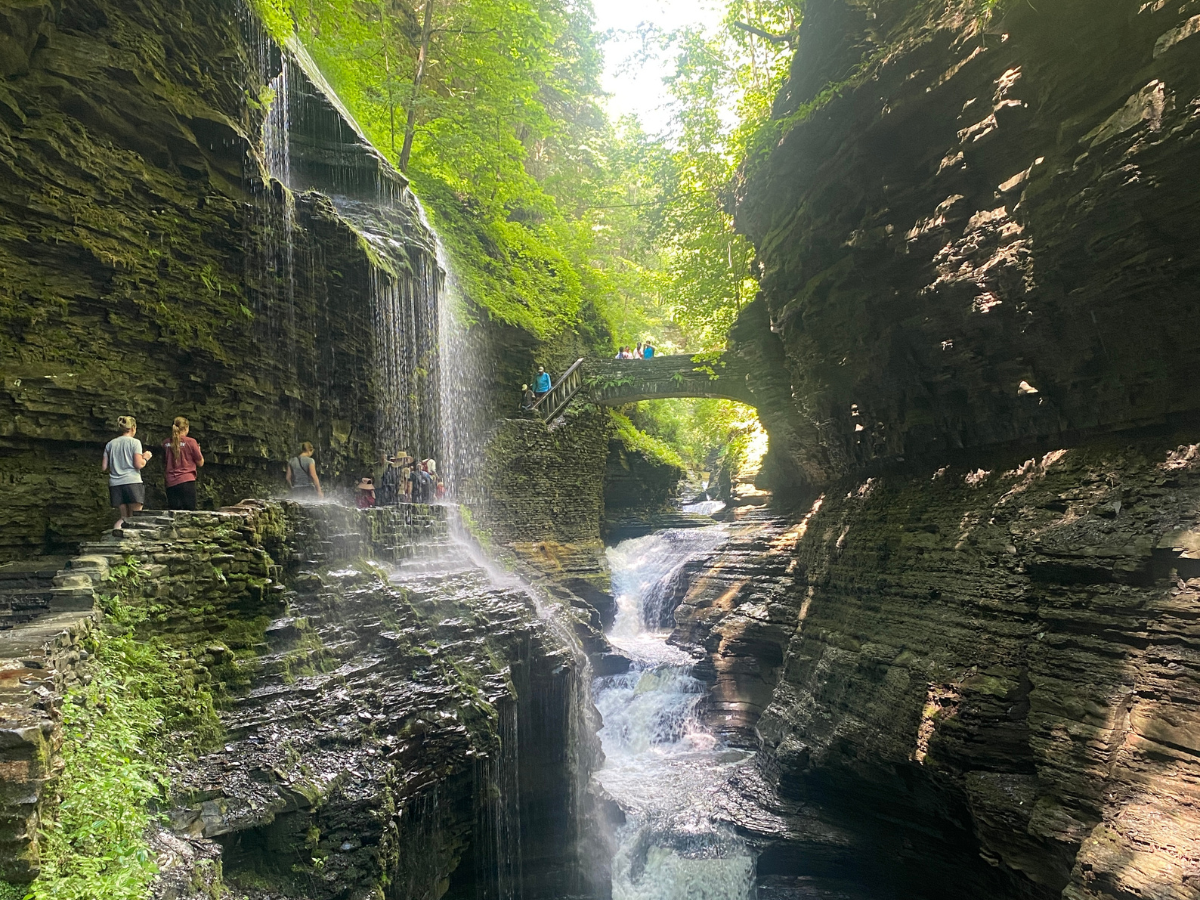 Water falling overhead of the a walkway with people walking underneath.