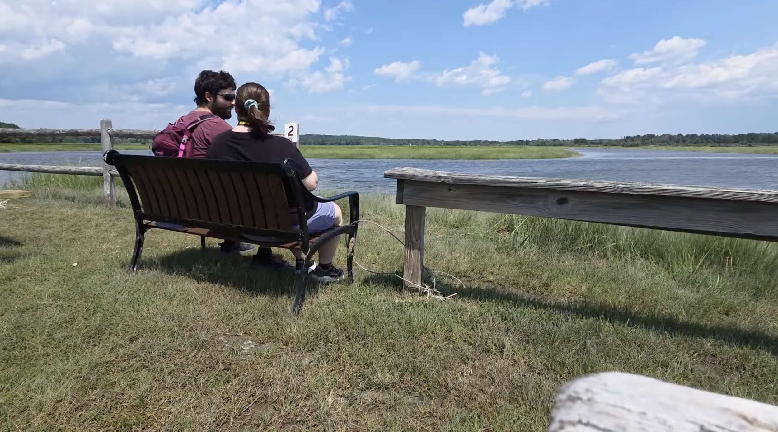 A couple sitting on a bench looking at the marsh.