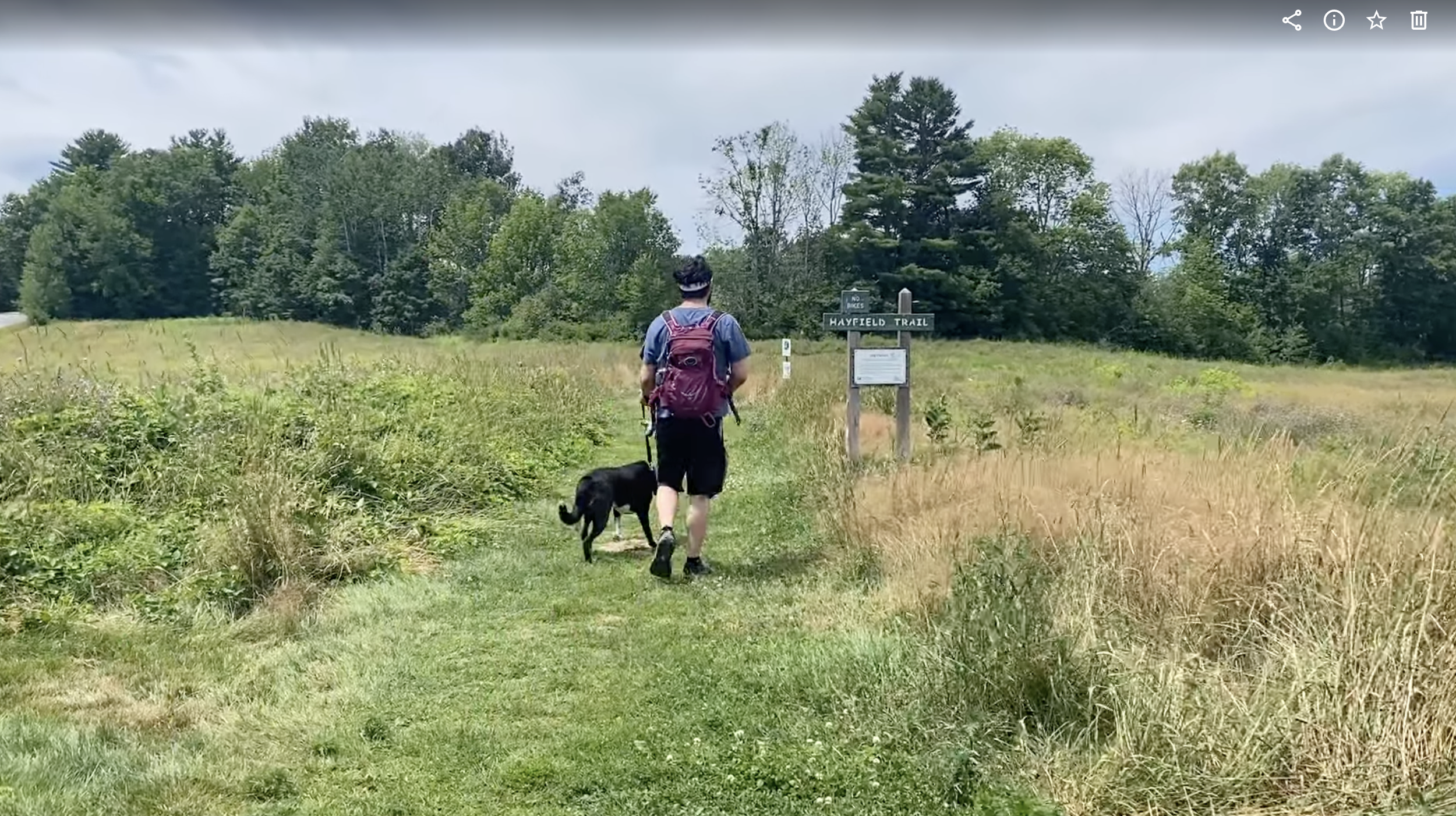 A man walking along the trail with a black dog. 