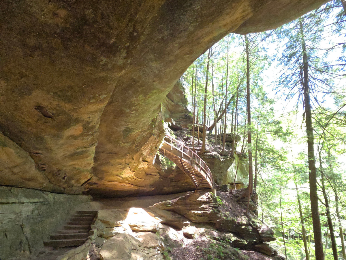 A rock formation extending over a walkway with trees off to the right
