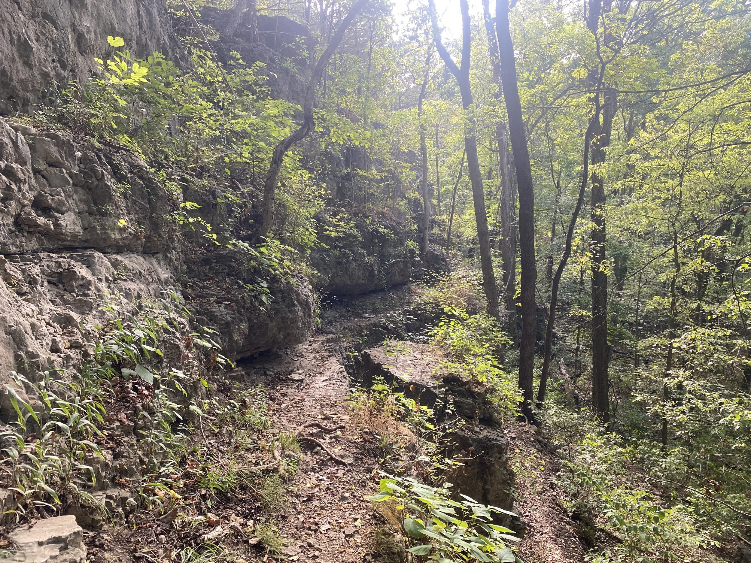 A rock formation is on the leftside of a path, and the right of the path drops off to a lower elevation area.
