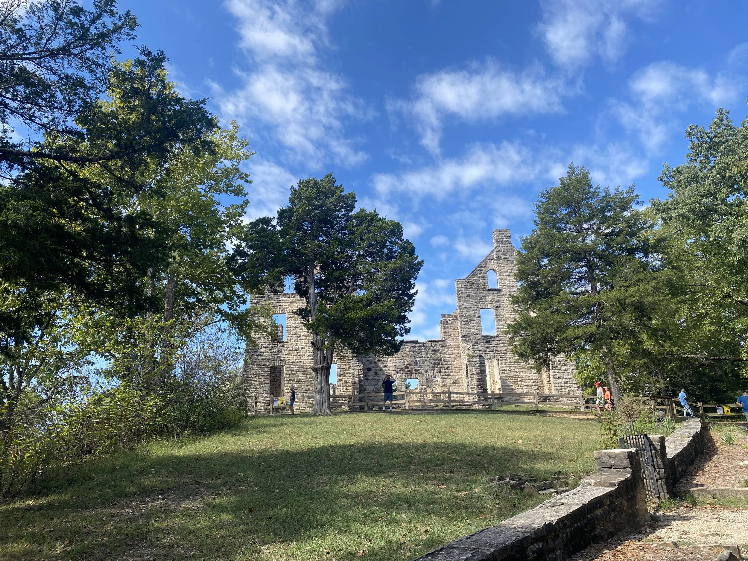 A deteriorating castle with several trees and a well manicured lawn in front of it.