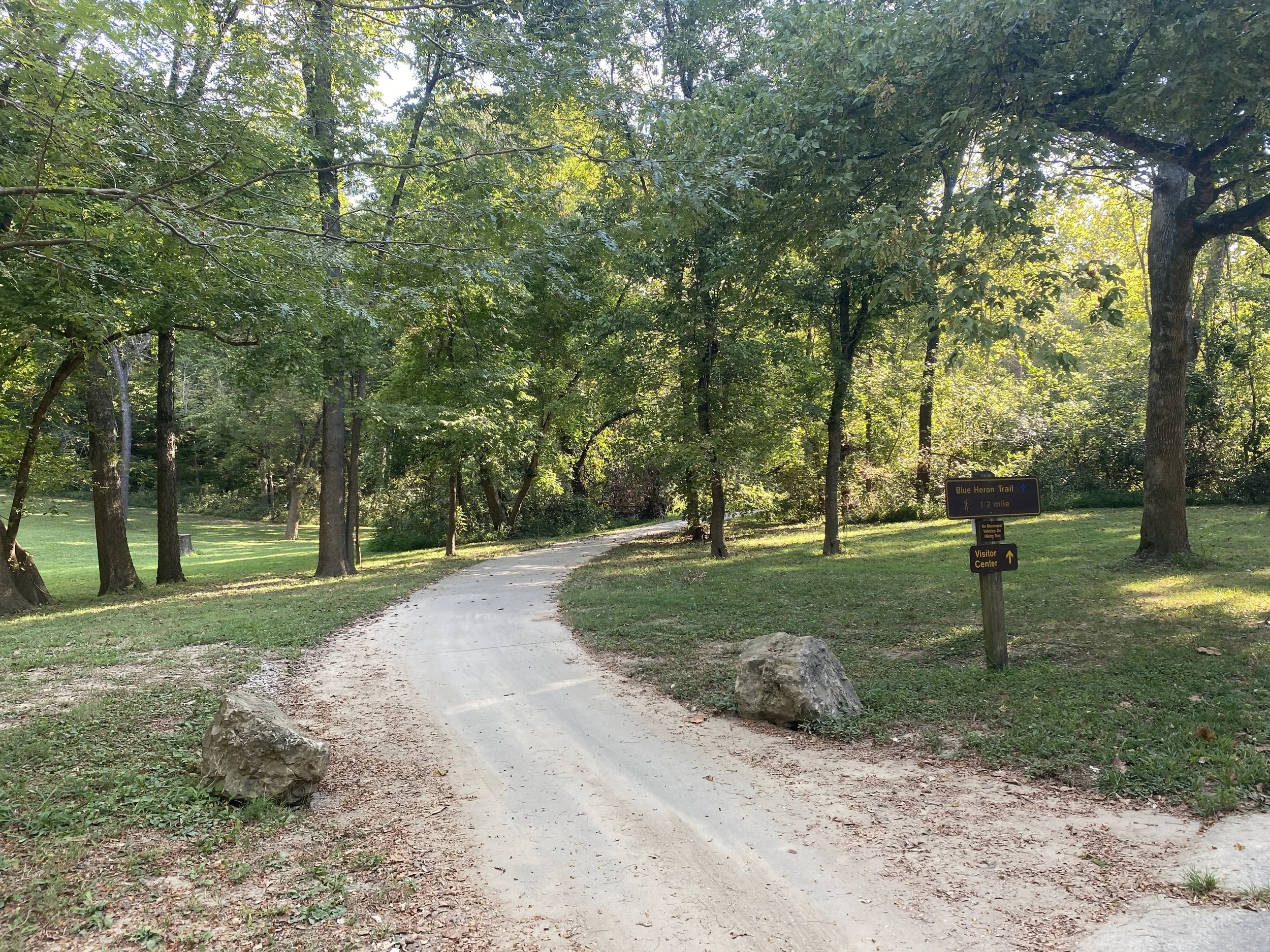 A gravel path with a sign for the trail with trees in the background.