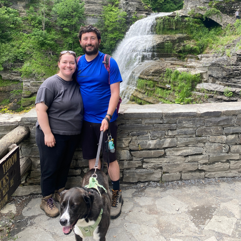 A couple with a dog pose in front of a waterfall.