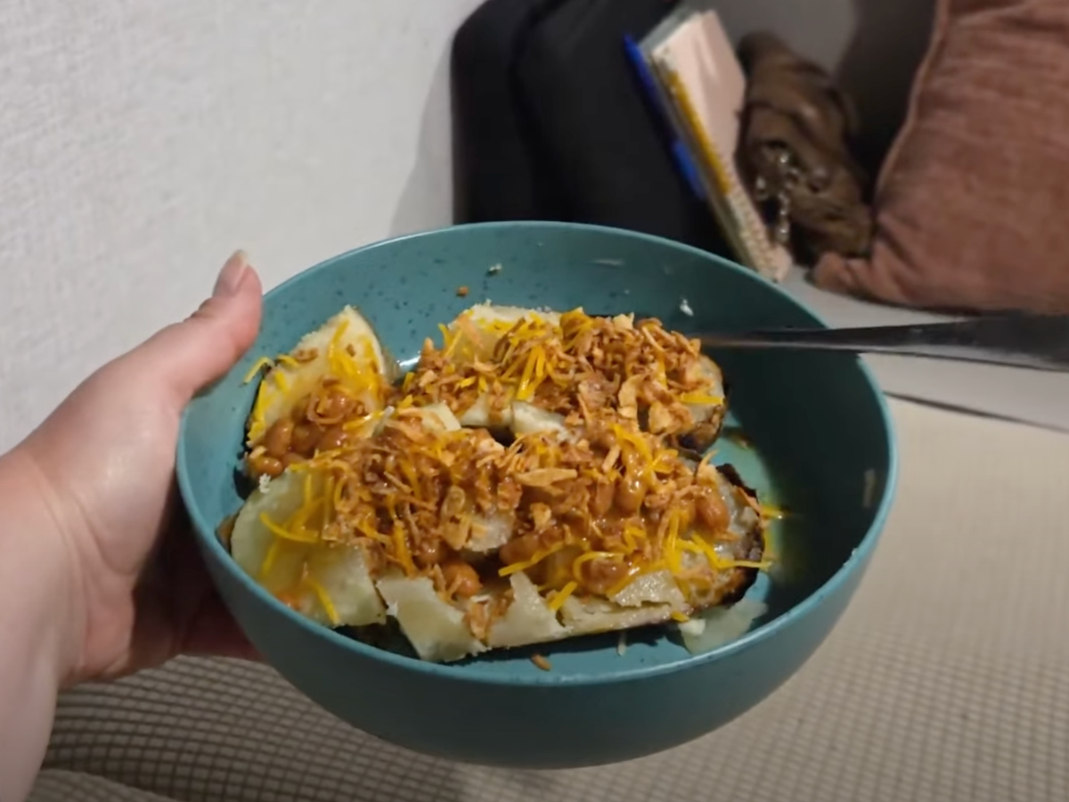 Bowl with loaded baked potato cut up with beans, cheese, and crunchy onions on top.
