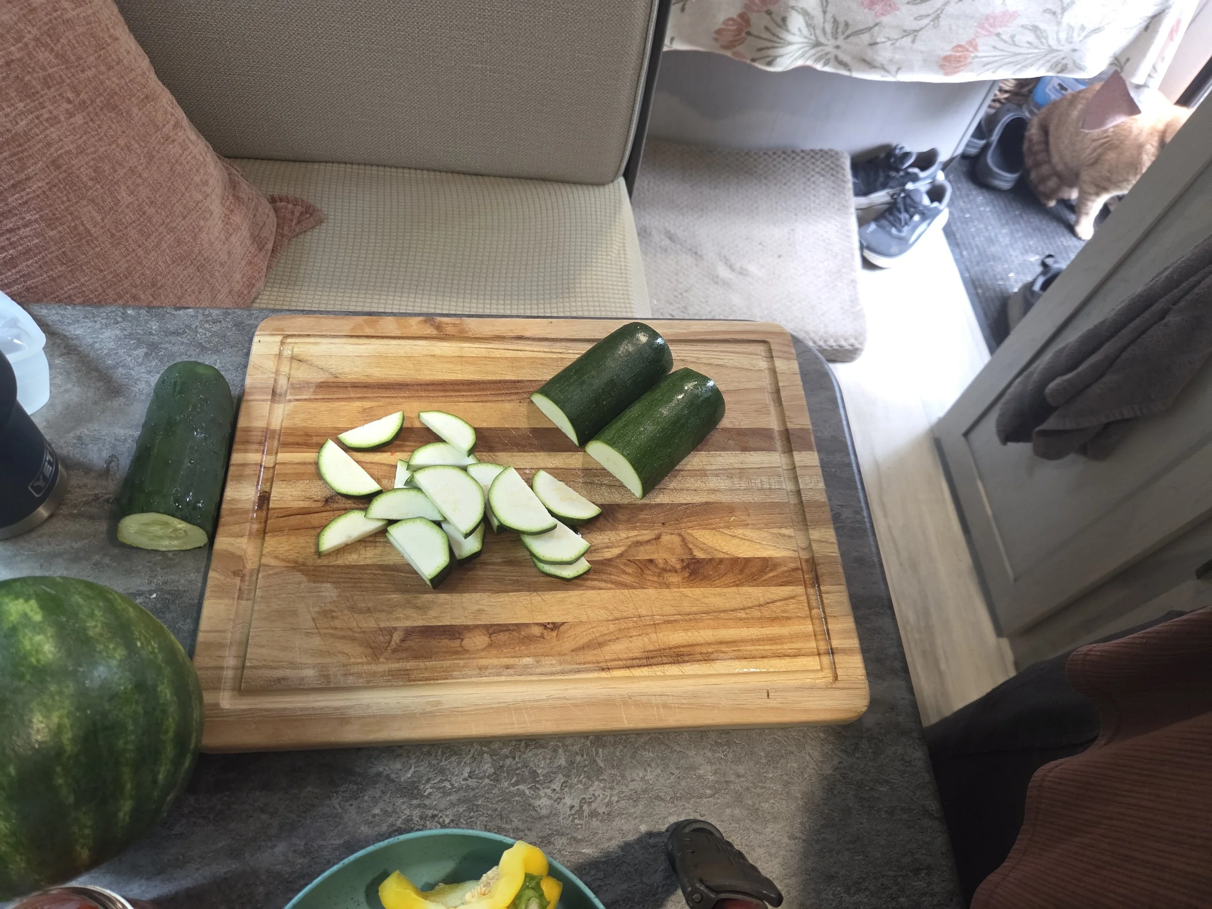 Wooden cutting board with a zucchini, partially sliced.