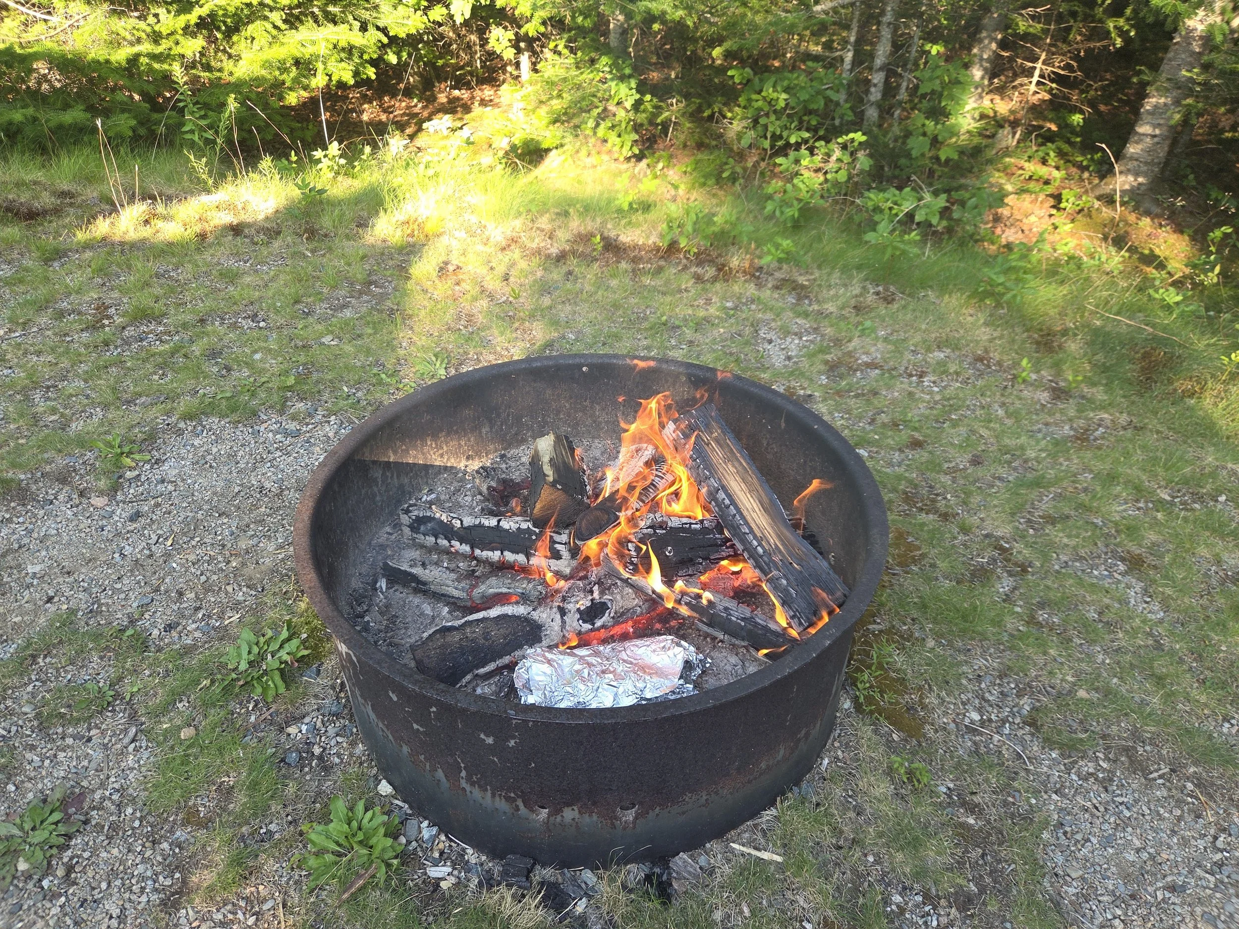 Roaring fire with two foil packets cooking inside the fire ring.