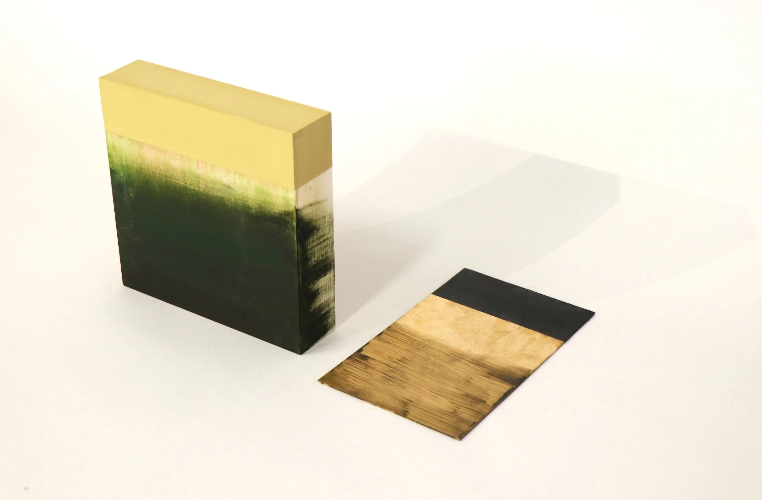 A small, rectangular, abstract photo frame with a gradient of yellow, green, and black, and an attached wooden panel with black edges on a white surface.