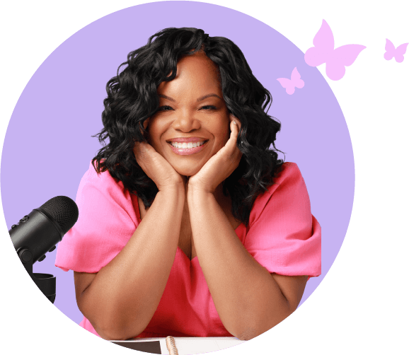 Nicole Gray smiling at her desk with a podcast microphone, wearing a pink top, symbolizing her Shine AF podcast and confidence coaching brand.