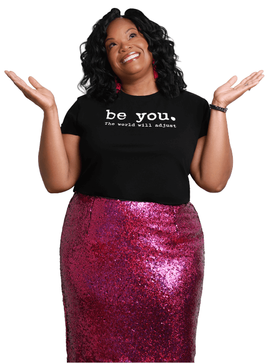 Nicole Gray smiling with arms raised in a playful question pose, wearing a “Be You” t-shirt and sequin skirt, representing her confidence coaching brand.