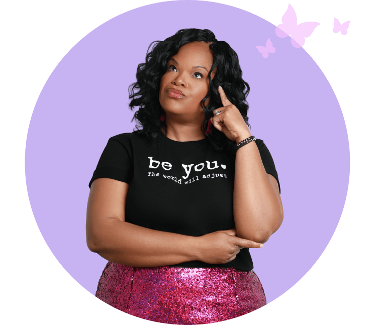 Nicole Gray in a “Be You” t-shirt and sequin skirt, looking thoughtful with hand on chin, representing reflection and mindset work in her confidence coaching.