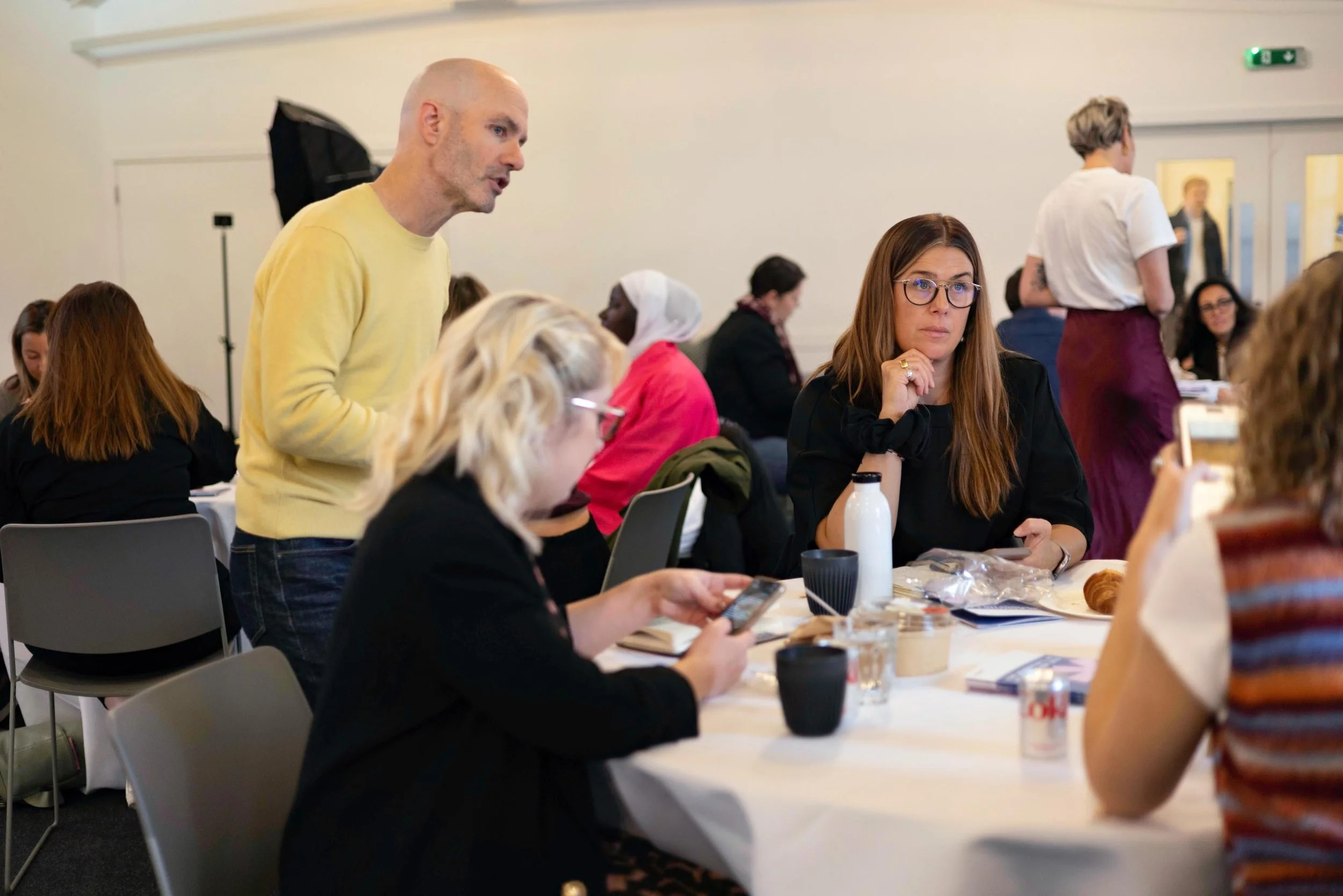 People sitting and standing around a conference table in a meeting or workshop room, engaged in discussion and activities.
