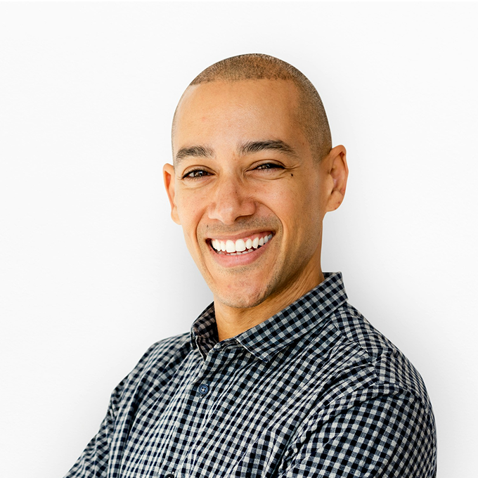 A smiling man with a shaved head wearing a checkered shirt, standing against a white background.