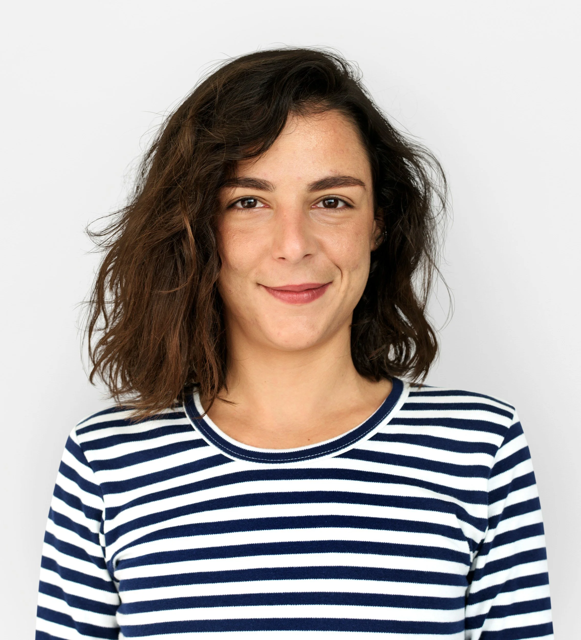 Close-up of a woman with wavy brown hair wearing a navy and white striped shirt, smiling slightly, against a plain white background.