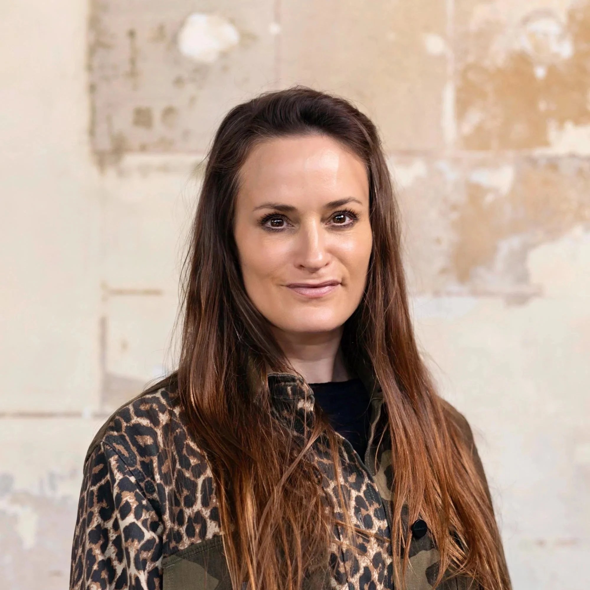 A woman with long brown hair and brown eyes wearing a leopard print jacket.