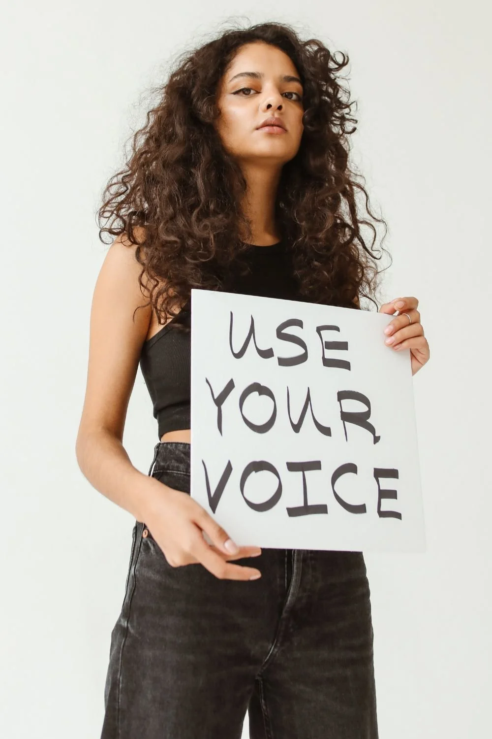 woman holding sign that reads "use your voice."  Photo by corelens on Canva.