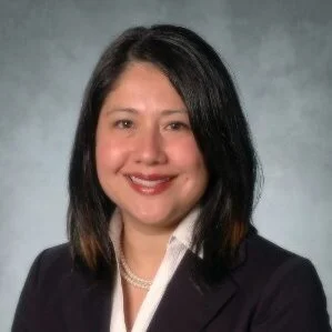 Headshot of a young Latina with a black bob hairstyle, smiling and wearing a black blazer, white collared shirt, and pearl necklace