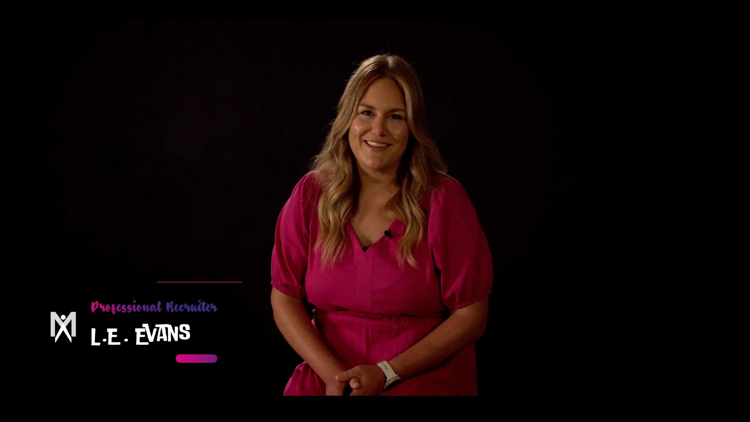 A woman in a pink dress sitting against a black background, smiling at the camera, with text overlay reading "Professional Recruiter L.E. Evans."
