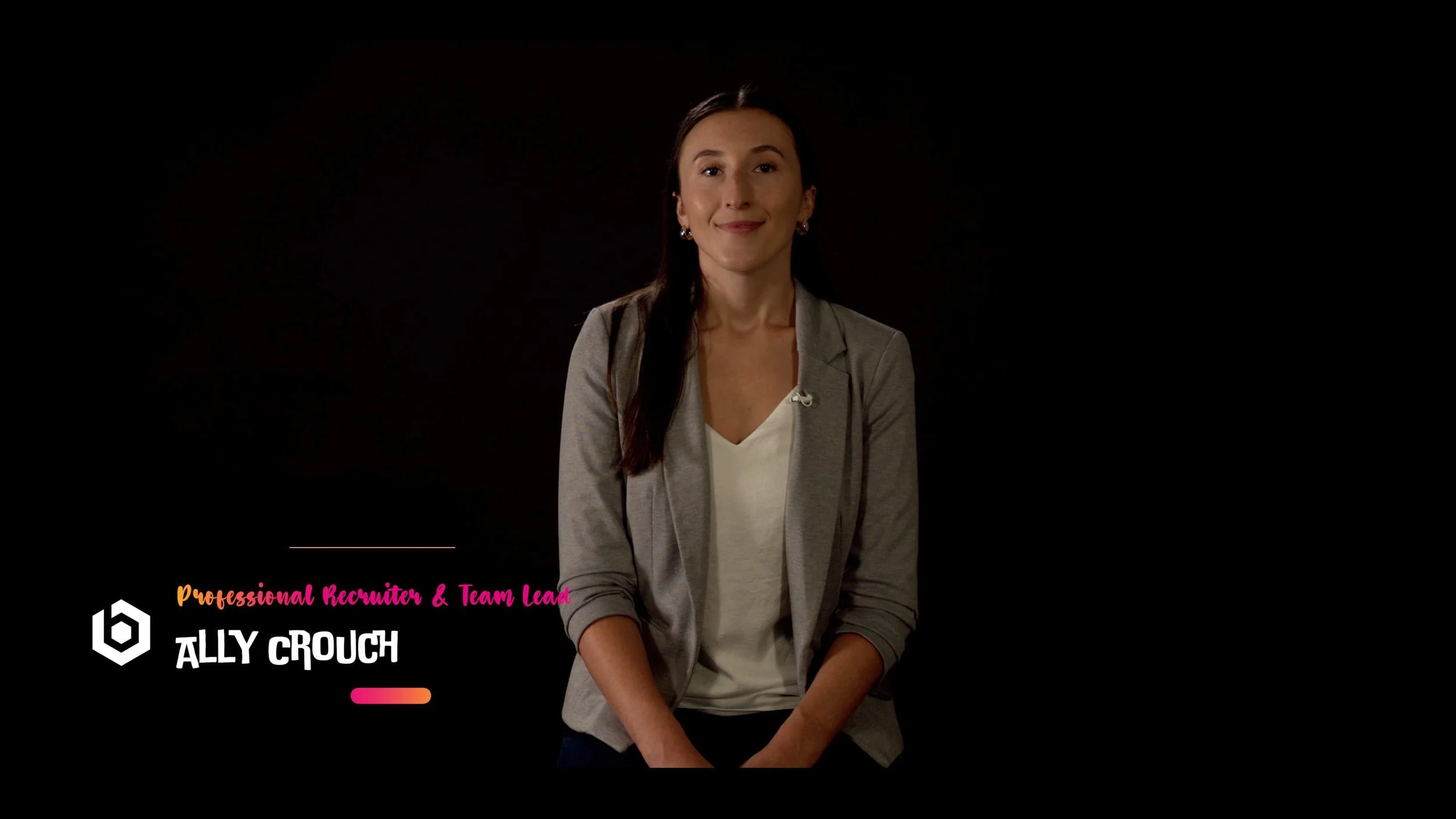 A woman with long dark hair tied to one side, wearing a gray blazer over a white blouse, sitting against a black background, with colorful text in the lower left corner that reads 'Professional Recruiter & Team Lead ALLY CROUCH'.