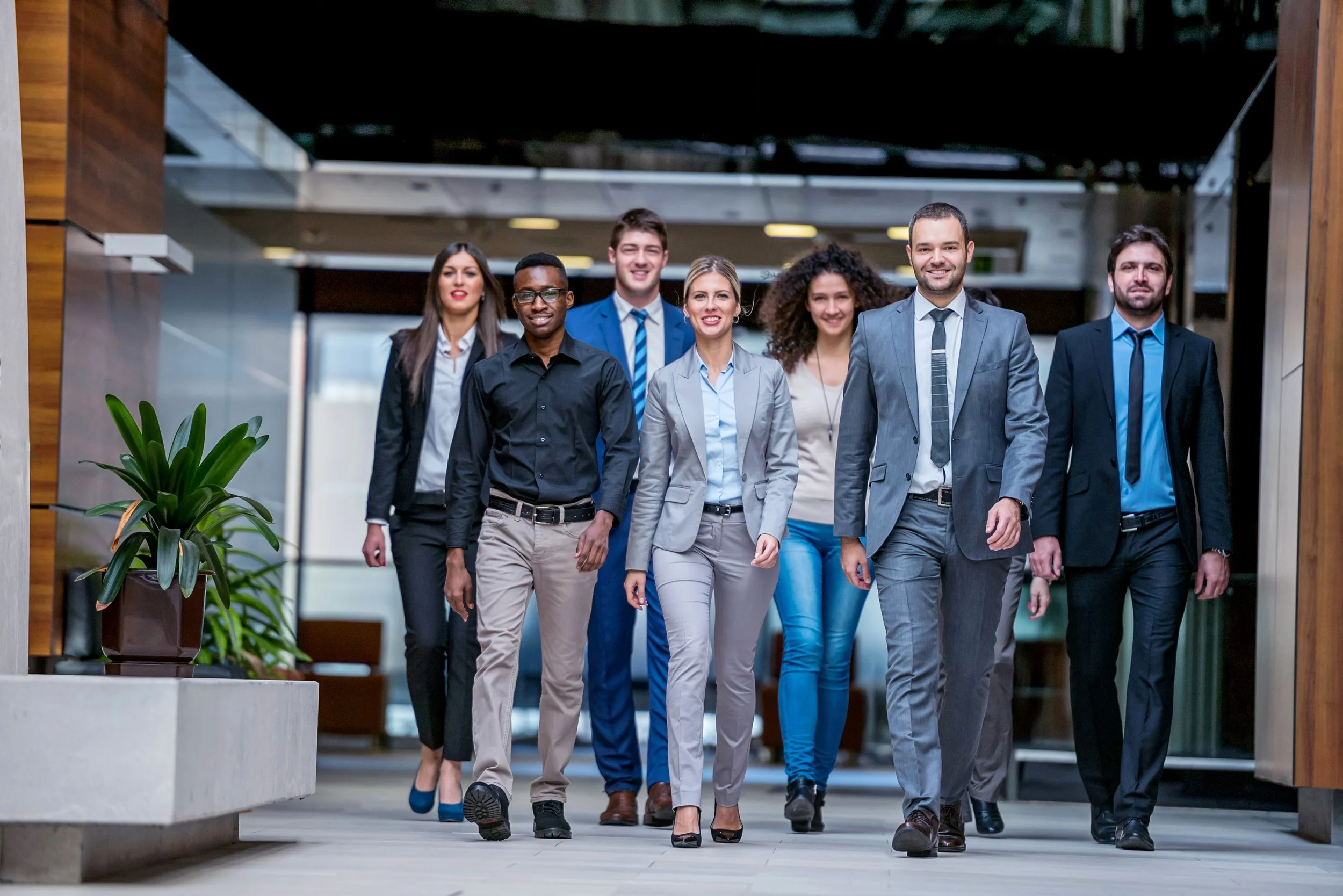 Group of seven diverse business professionals walking confidently in a modern office lobby.