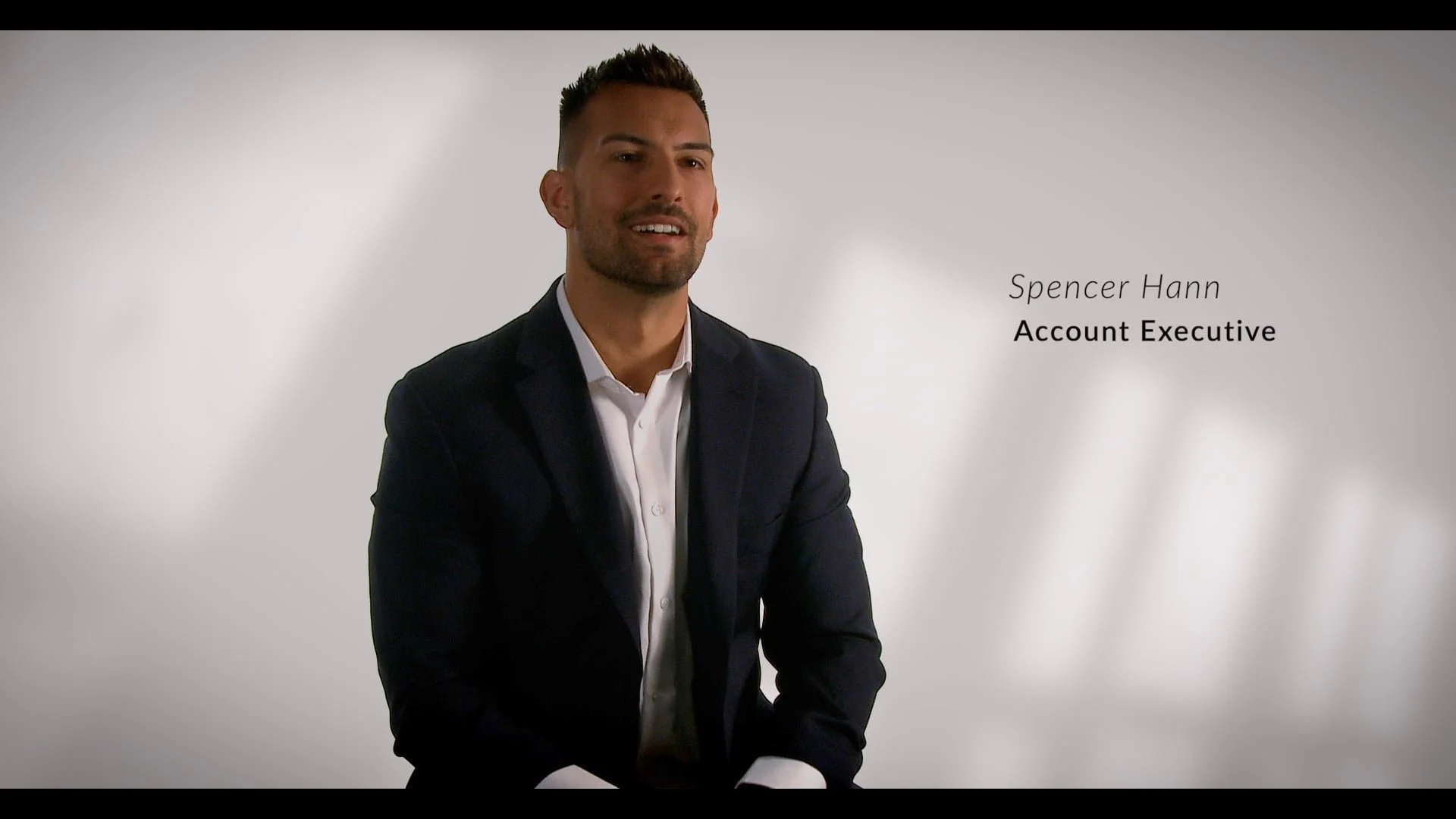 A professional man in a dark suit and white shirt sitting against a neutral background, with the text 'Spencer Hann, Account Executive' appearing beside him.