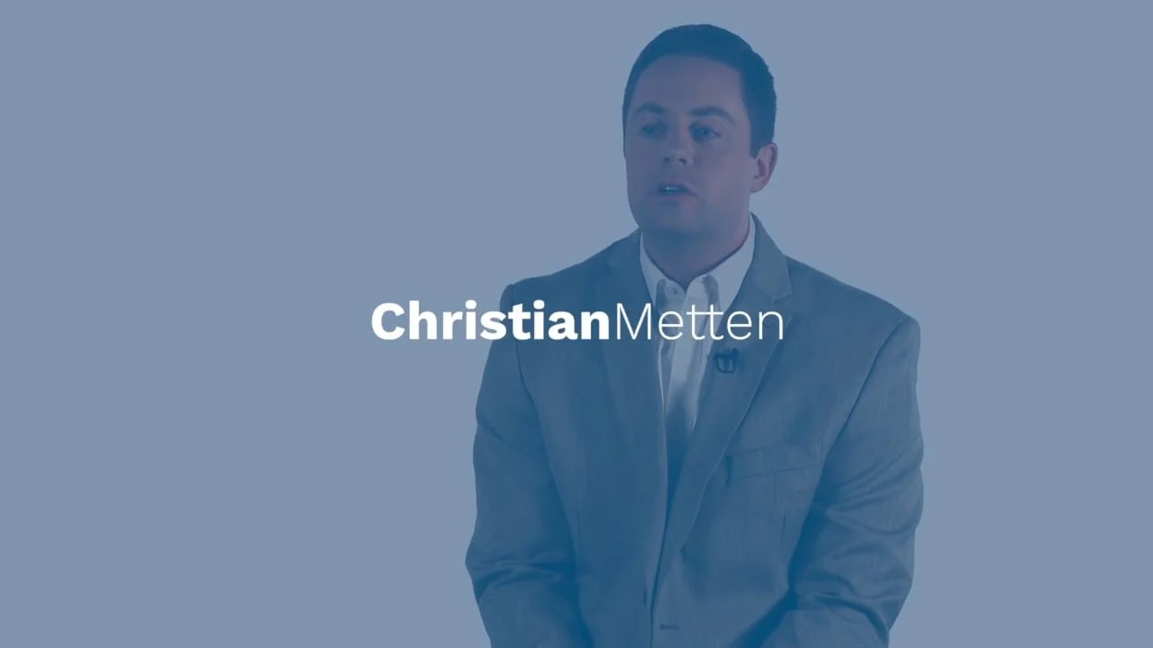 A man in a gray suit sitting against a blue background with the name Christian Metten overlayed.