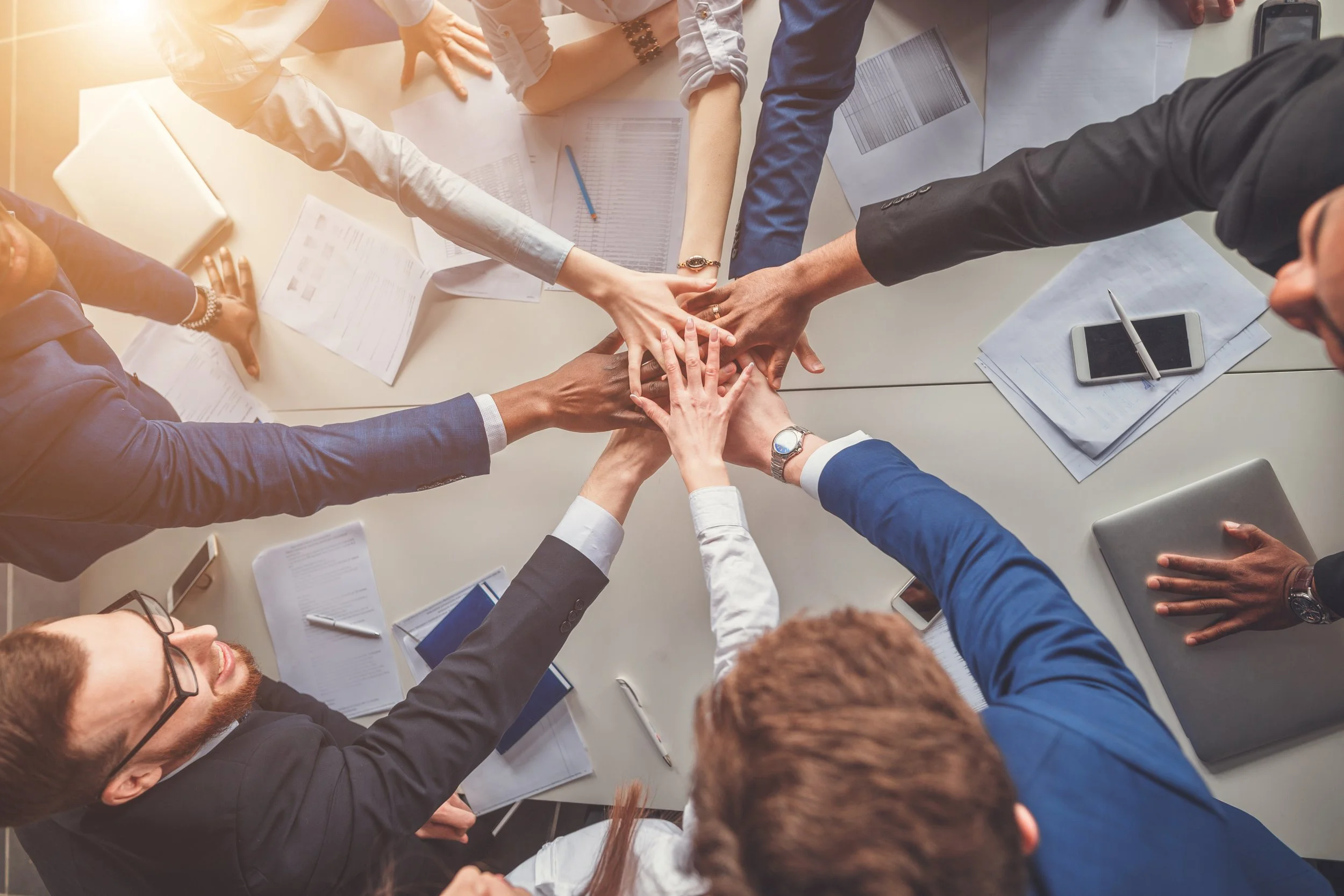 A top-down view of a diverse group of businesspeople putting their hands together in a circle over a conference table.