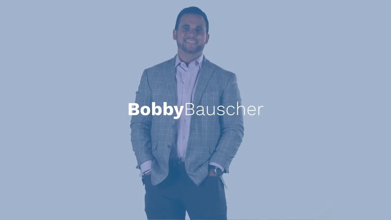 A man in a gray checked blazer and light purple shirt smiling, with the text "Bobby Bauscher" overlayed.