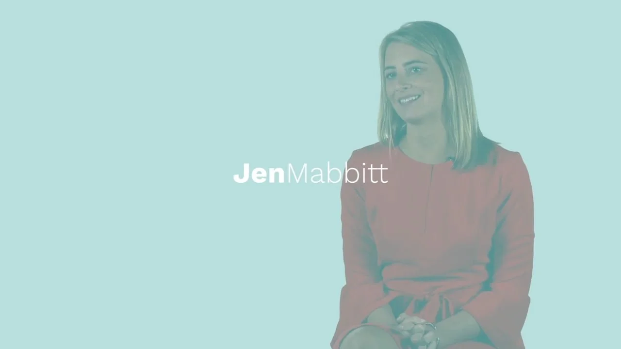 A woman with shoulder-length blonde hair, wearing a red dress, sitting with her hands clasped, smiling, with the text "Jen Mabbitt" overlayed on a light blue background.