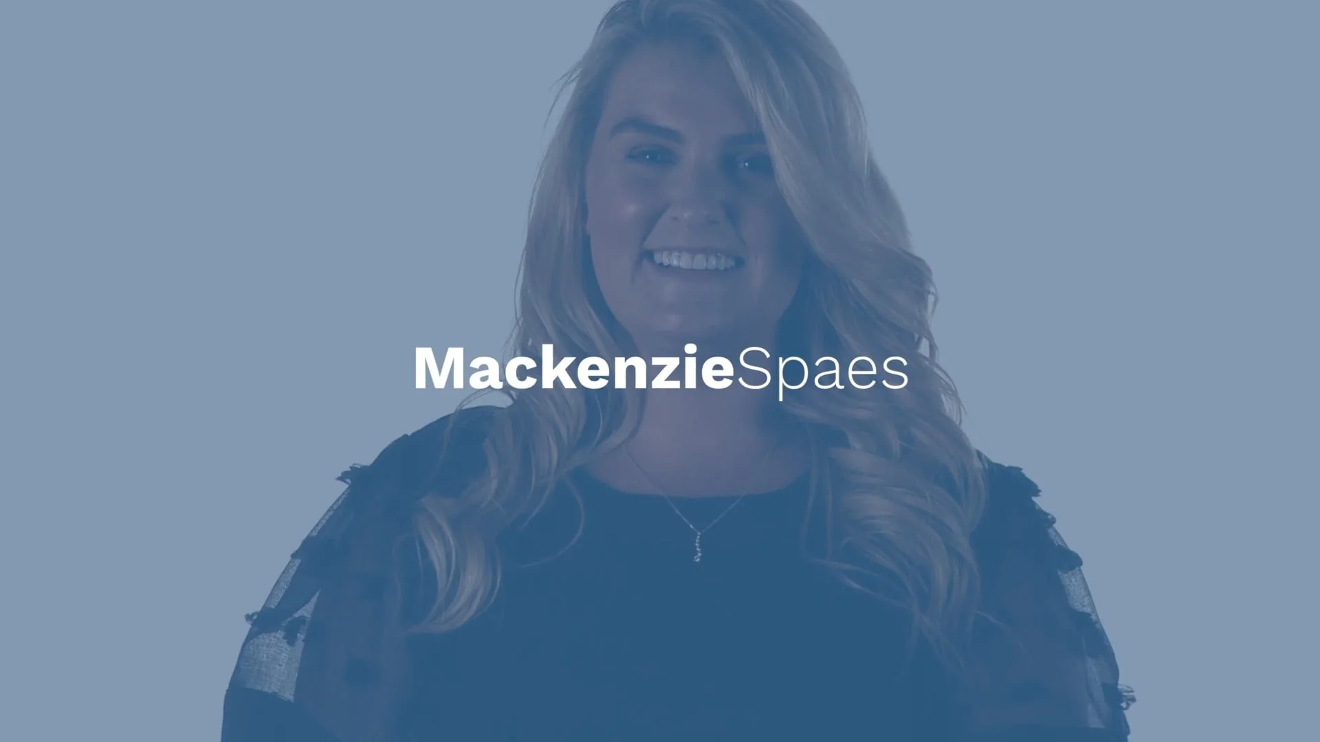 A smiling woman with wavy blonde hair, wearing a dark top and a delicate necklace, against a light blue background with her name, Mackenzie Spaes, written across her chest.