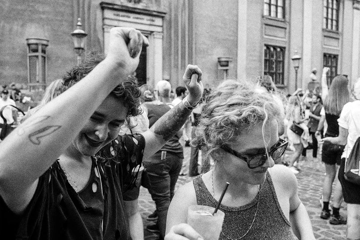 Two women dancing and having fun among a crowd of people outside in a city street.