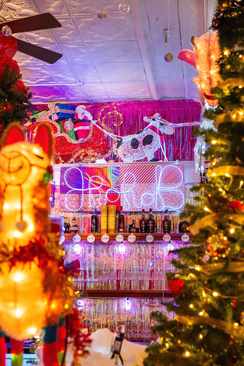Decorated Christmas display with a neon sign saying 'Ho Ho Ho,' Christmas trees, presents, and holiday lights in a festive setting.