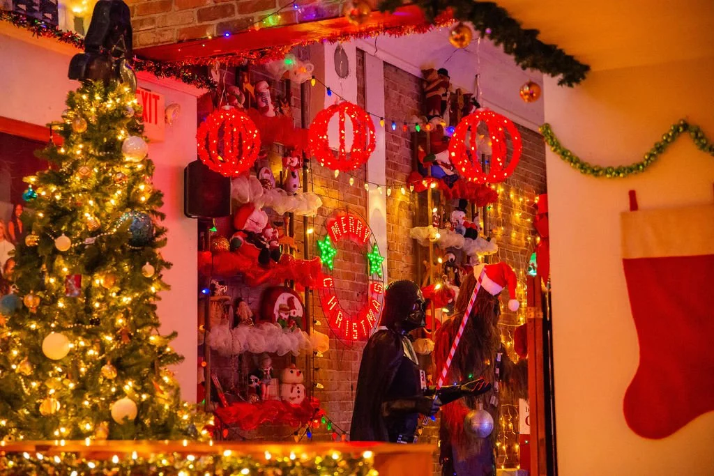 Decorated Christmas display with a Christmas tree, ornaments, lights, Santa figurines, stockings, and holiday decorations in a festive room.