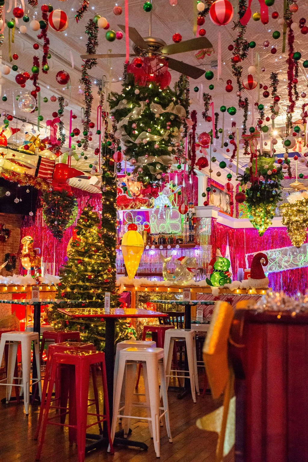 Decorated Christmas inside a festive venue with hanging ornaments, Christmas trees, colorful lights, and holiday decorations.