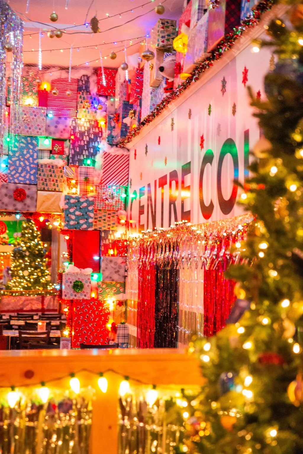 Colorful Christmas decorations with many wrapped presents, string lights, and Christmas trees at a festive location.