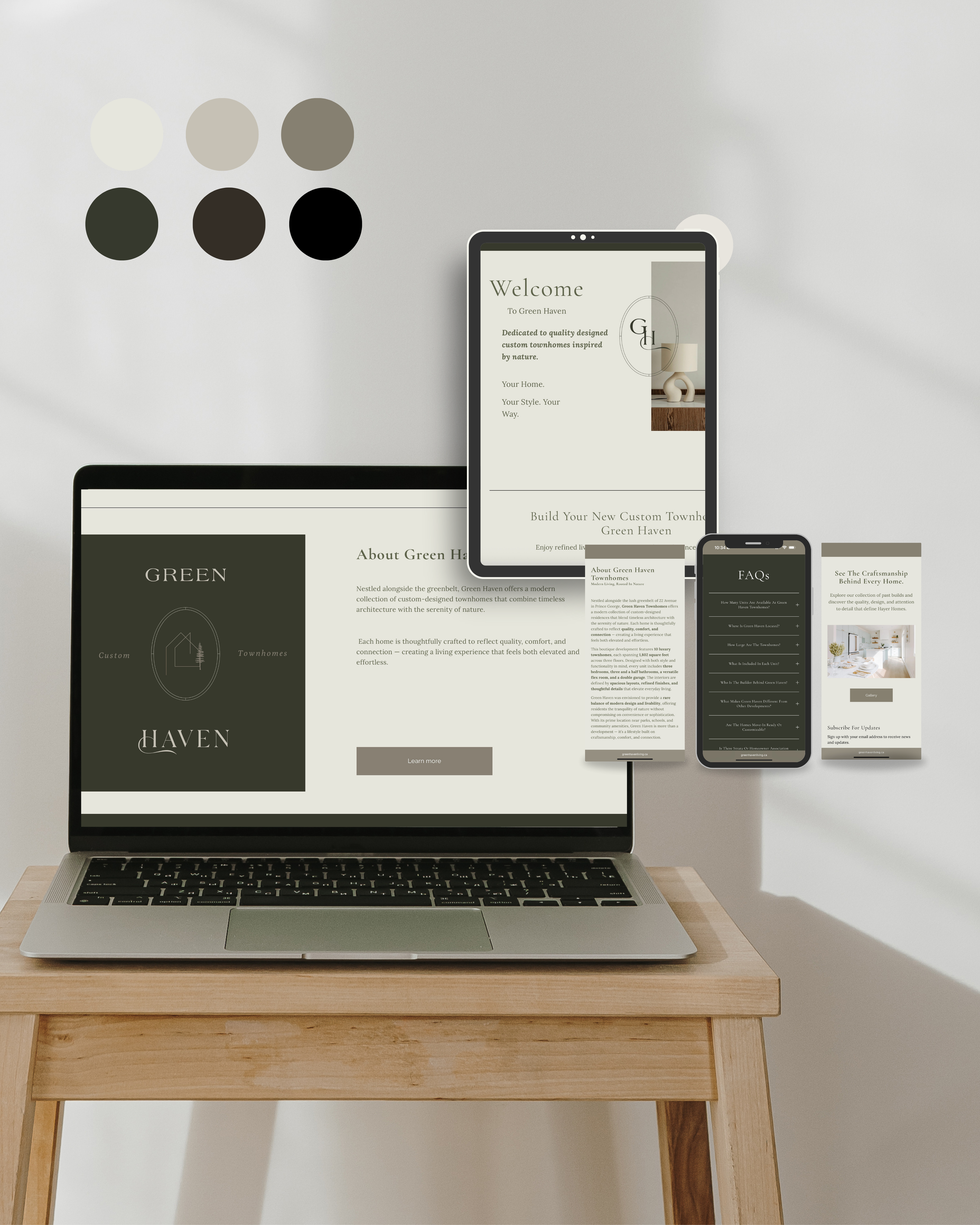 Laptop and smartphone displaying website mockups for Green Haven, a company specializing in custom townhomes, on a wooden table with color palette samples on a white wall.