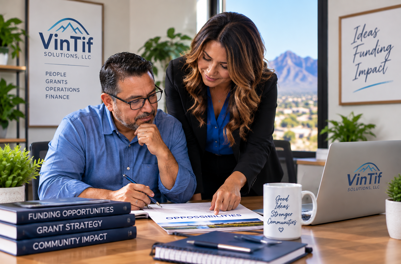 Two women discussing documents in an office with a mountain view. One woman is seated, wearing glasses and a blue shirt, holding a pen, while the other woman is leaning over, pointing at a paper. There are stacked books titled Funding Opportunities, Grant Strategy, and Community Impact on the table, a laptop with the VinTif Solutions LLC logo, a coffee mug with the words Good Ideas, Stronger Communities, and some potted plants. A whiteboard in the background mentions ideas, funding, and impact.