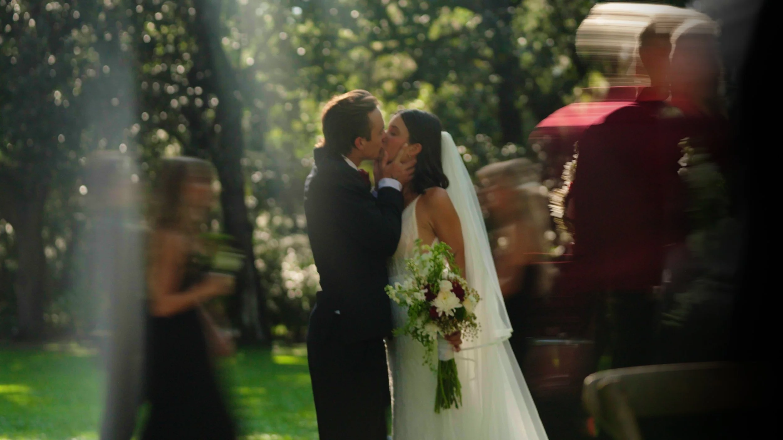 A bride and groom sharing a kiss at their outdoor wedding ceremony with guests blurred in the foreground.