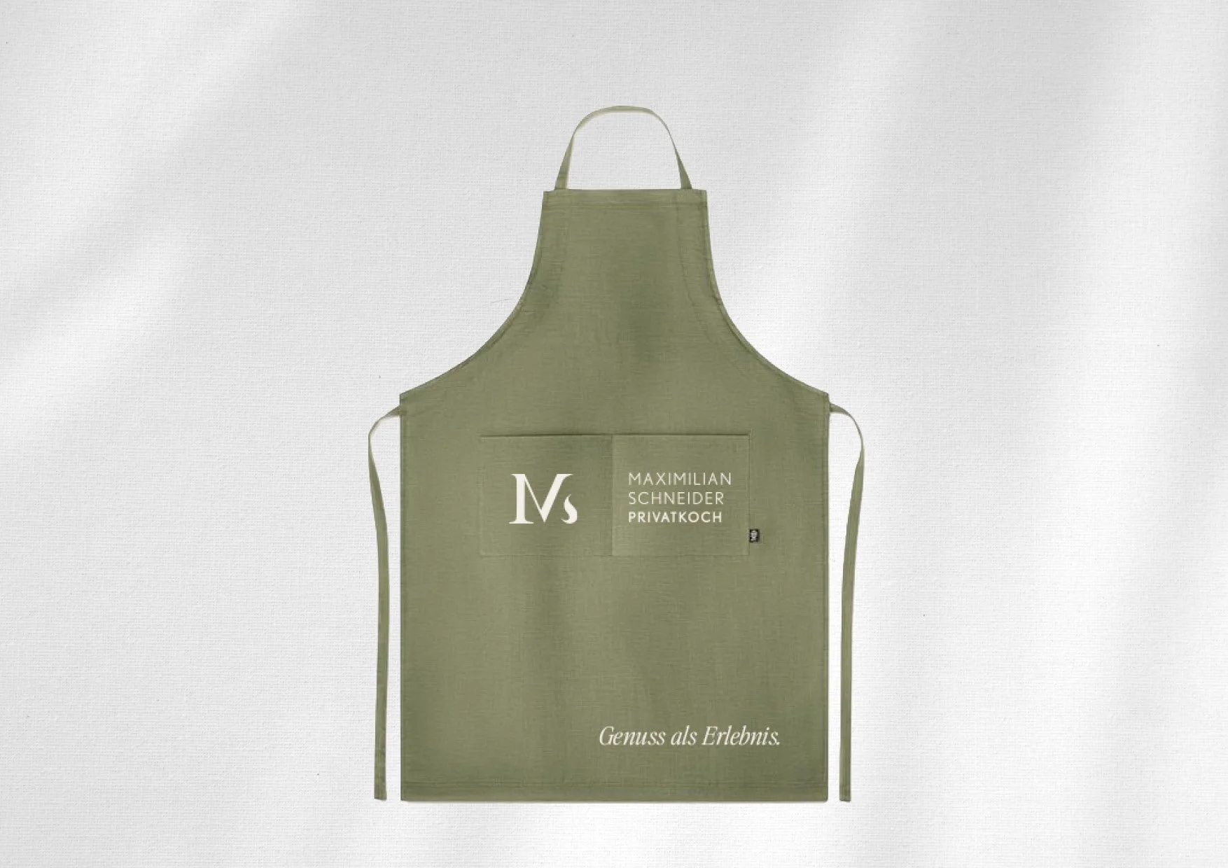 Branding für Privatkoch Maximilian Schneider: gebrandete Kochschürze mit Logo und Claim „Genuss als Erlebnis“.