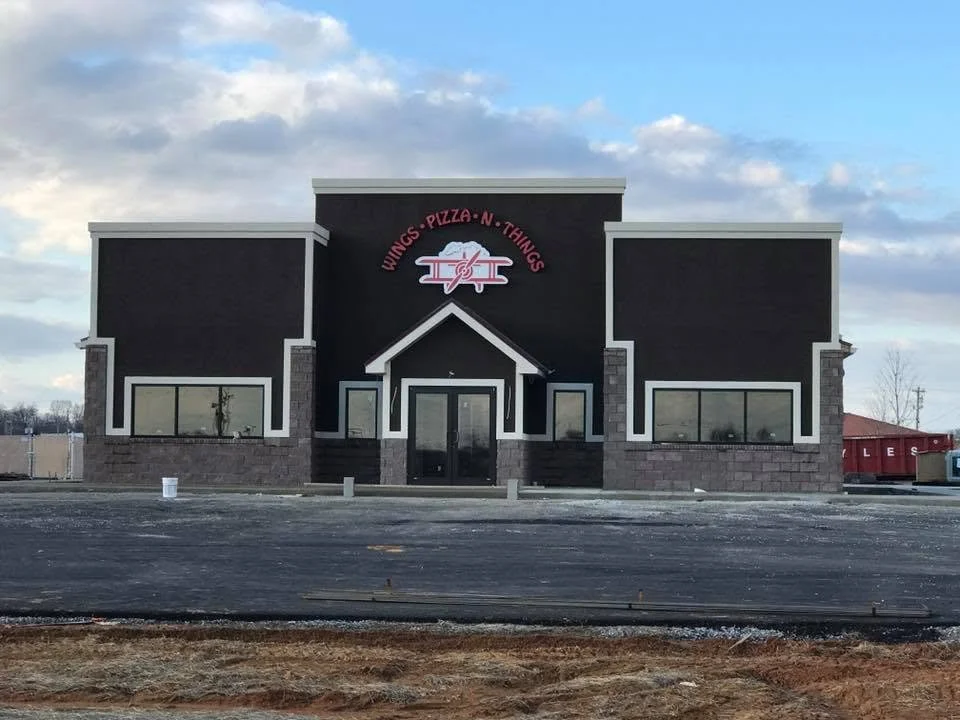 Exterior of a black-and-gray restaurant building with a wings, pizza, and things sign above the entrance.