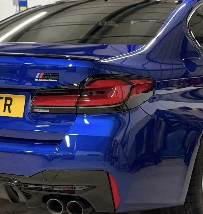 Close-up of the rear of a blue sports car with an M4 badge, four exhaust pipes, and a yellow license plate.