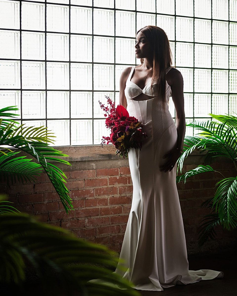 That moment when window light creates pure magic. The grid panes behind this bride create the most stunning silhouette, highlighting her elegant profile against that warm brick wall. I love how the light catches the edges of her gown while those vibr