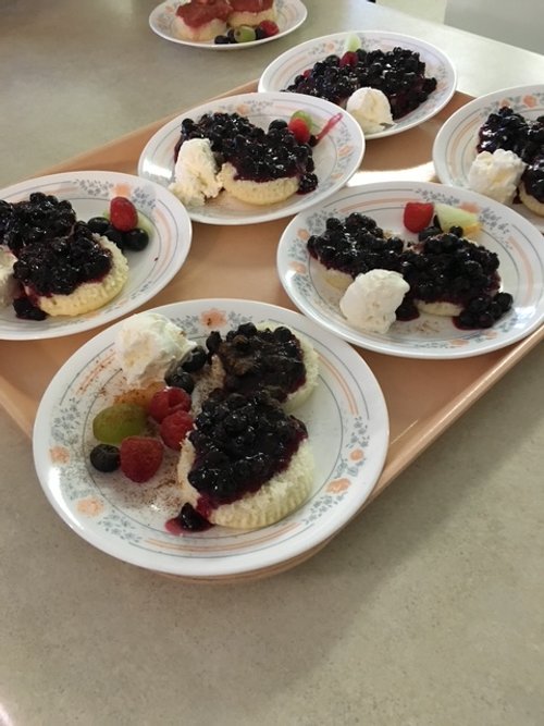 Plates of cheesecake topped with blueberry sauce, garnished with scoops of ice cream and assorted berries.