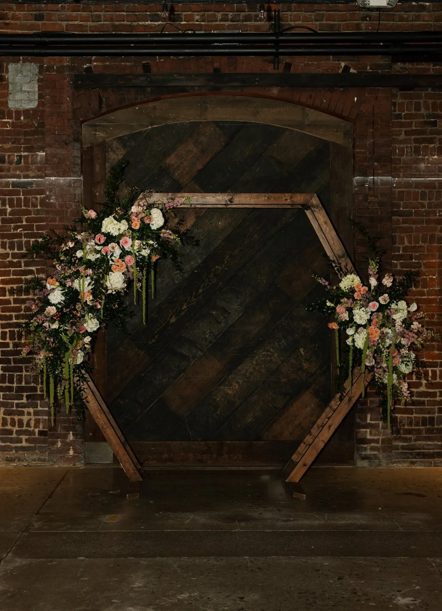 Rustic wooden ceremony backdrop with pink, white, and peach floral arrangements set against exposed brick inside Jackson Terminal in Knoxville.