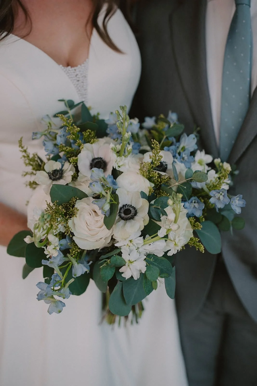 Bride and groom holding a white and blue wedding bouquet with roses, anemones, delphinium, and eucalyptus at Jackson Terminal in Knoxville, Tennessee.