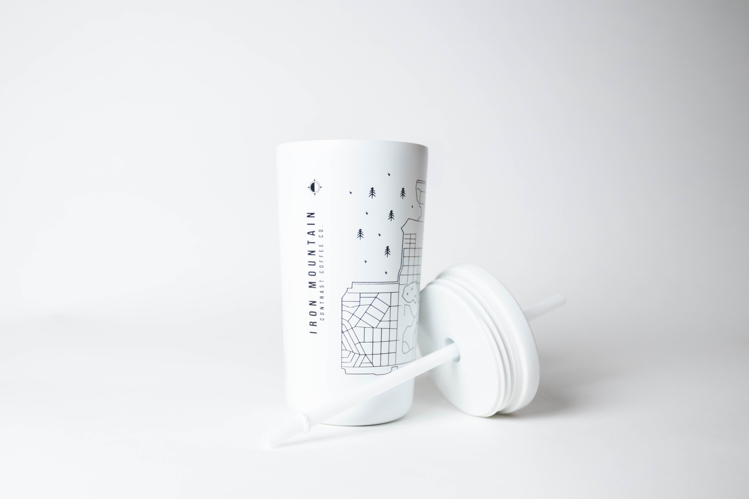White reusable cup with line drawing design and "Iron Mountain Contrast Coffee Co." text, shown with lid and straw on a white background.