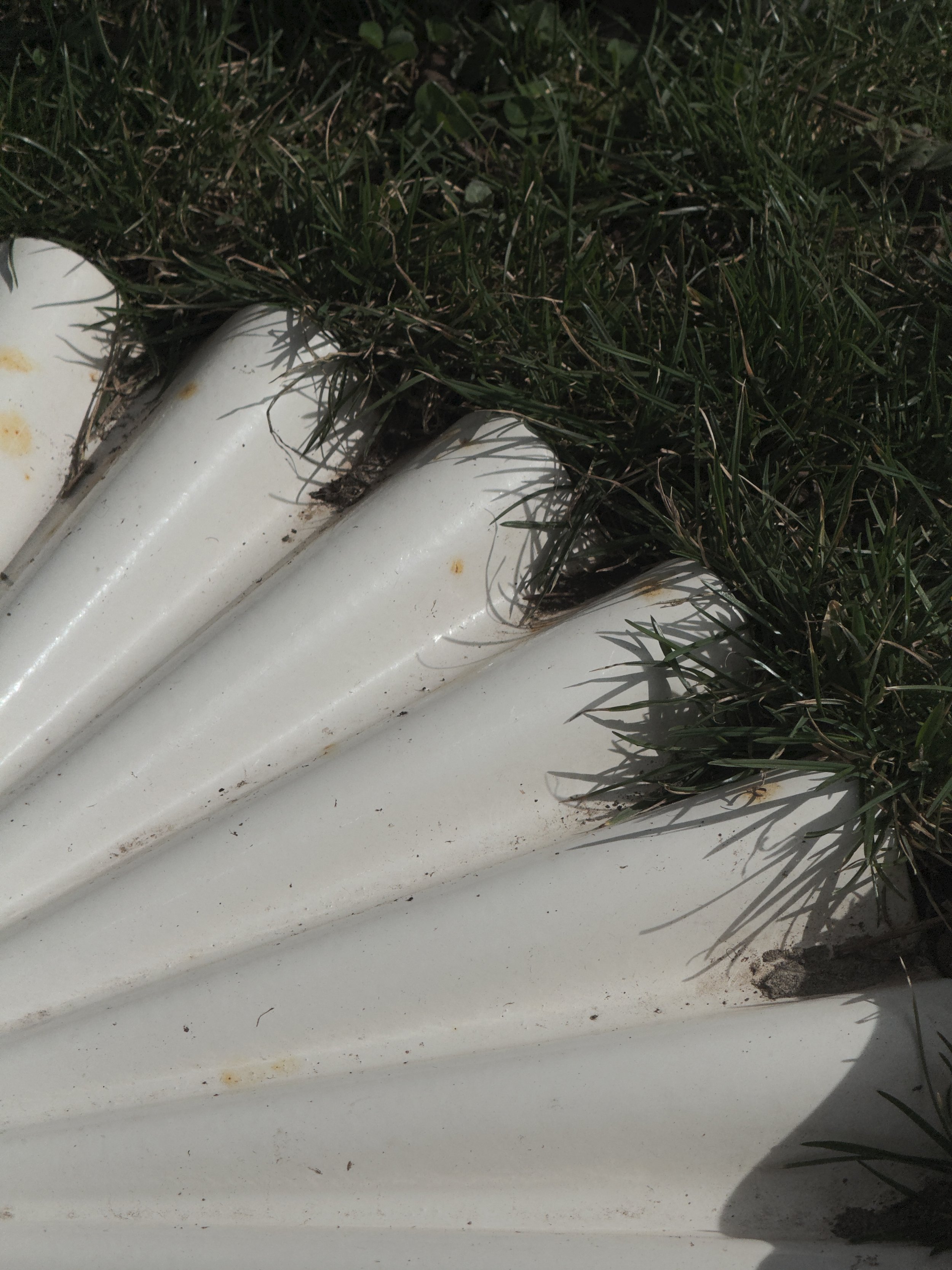 Close-up of a white garden edging or lawn border with grass growing over the top.