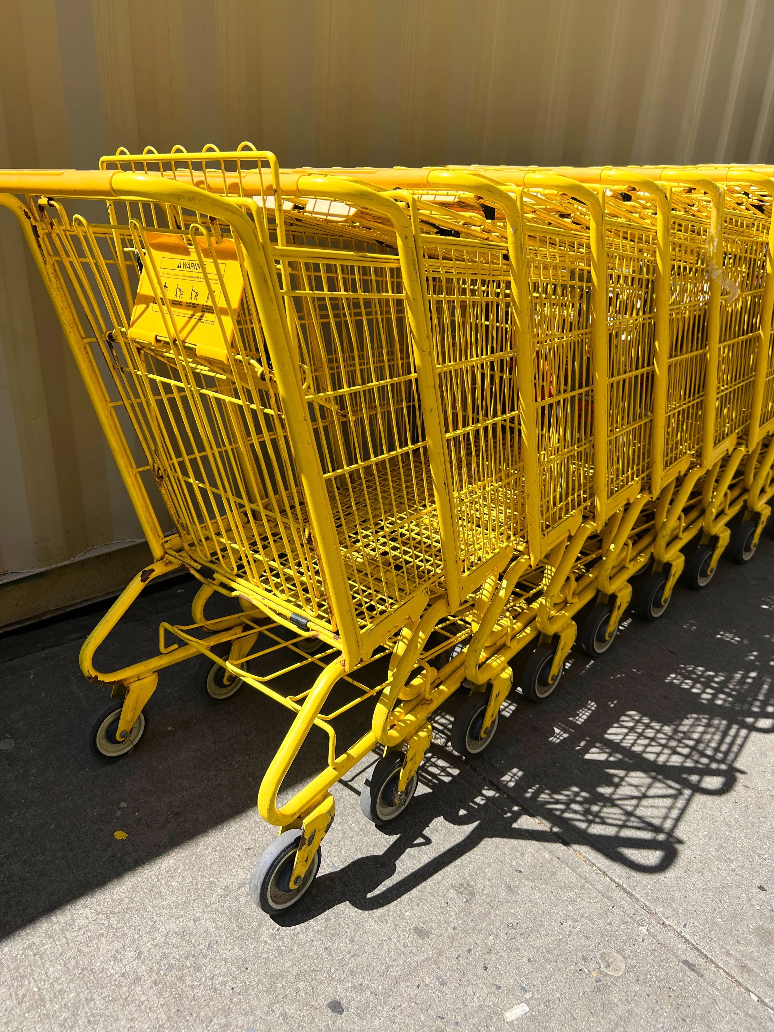 Multiple yellow shopping carts lined up outside on a sidewalk with shadow cast by the carts.